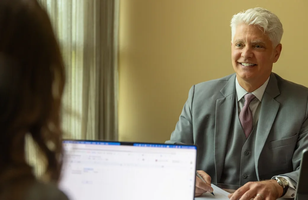 Attorney Grant Gehrmann smiling during a client consultation at his desk